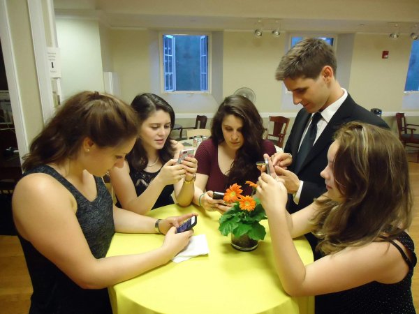 Five teens around a table at a social event all staring at there mobile phones.